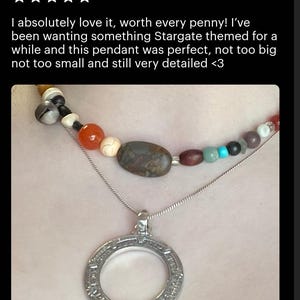 A handmade Stargate pendant necklace with a pendant featuring a circular design. The pendant is made of metal and has a stone-like appearance. The necklace is displayed on a person's neck, and the image is described as a review of the handmade pendant.