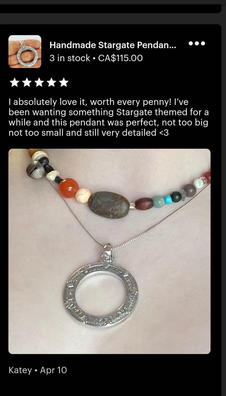 A handmade Stargate pendant necklace with a pendant featuring a circular design. The pendant is made of metal and has a stone-like appearance. The necklace is displayed on a person's neck, and the image is described as a review of the handmade pendant.