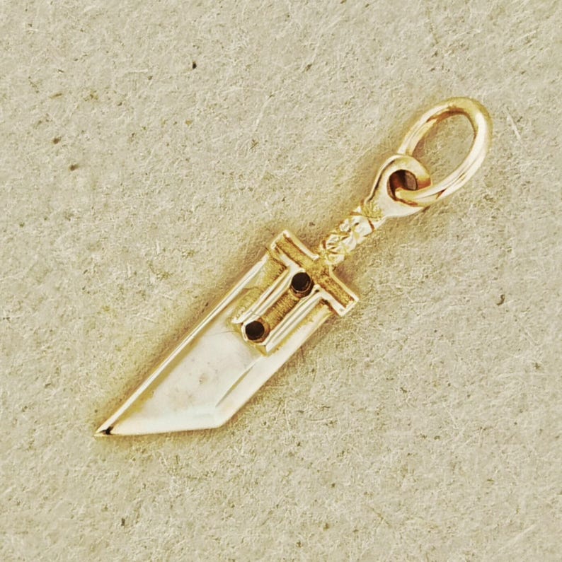 Antique bronze Cloud Strife sword charm from FFVII Final Fantasy gamer jewelry. Small FF7 Buster Sword charm in antique bronze Final Fantasy Cloud Strife pendant. Close up of small Buster Sword pendant in bronze FF7 inspired cosplay accessory. Mini Final Fantasy sword charm in bronze Cloud Strife cosplay gift.