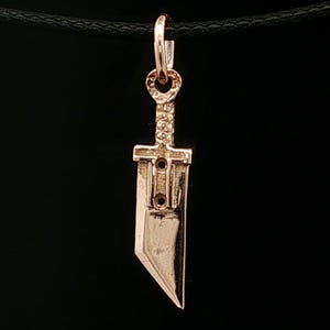 Antique bronze Cloud Strife sword charm from FFVII Final Fantasy gamer jewelry. Small FF7 Buster Sword charm in antique bronze Final Fantasy Cloud Strife pendant. Close up of small Buster Sword pendant in bronze FF7 inspired cosplay accessory. Mini Final Fantasy sword charm in bronze Cloud Strife cosplay gift