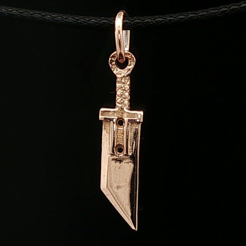 Antique bronze Cloud Strife sword charm from FFVII Final Fantasy gamer jewelry. Small FF7 Buster Sword charm in antique bronze Final Fantasy Cloud Strife pendant. Close up of small Buster Sword pendant in bronze FF7 inspired cosplay accessory. Mini Final Fantasy sword charm in bronze Cloud Strife cosplay gift