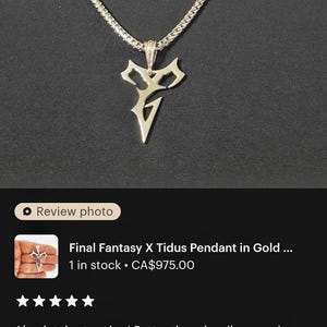 a close-up view of a gold necklace with a pendant featuring a stylized letter "V" design. The necklace is displayed on a person's neck, and the image appears to be a review photo of the necklace.