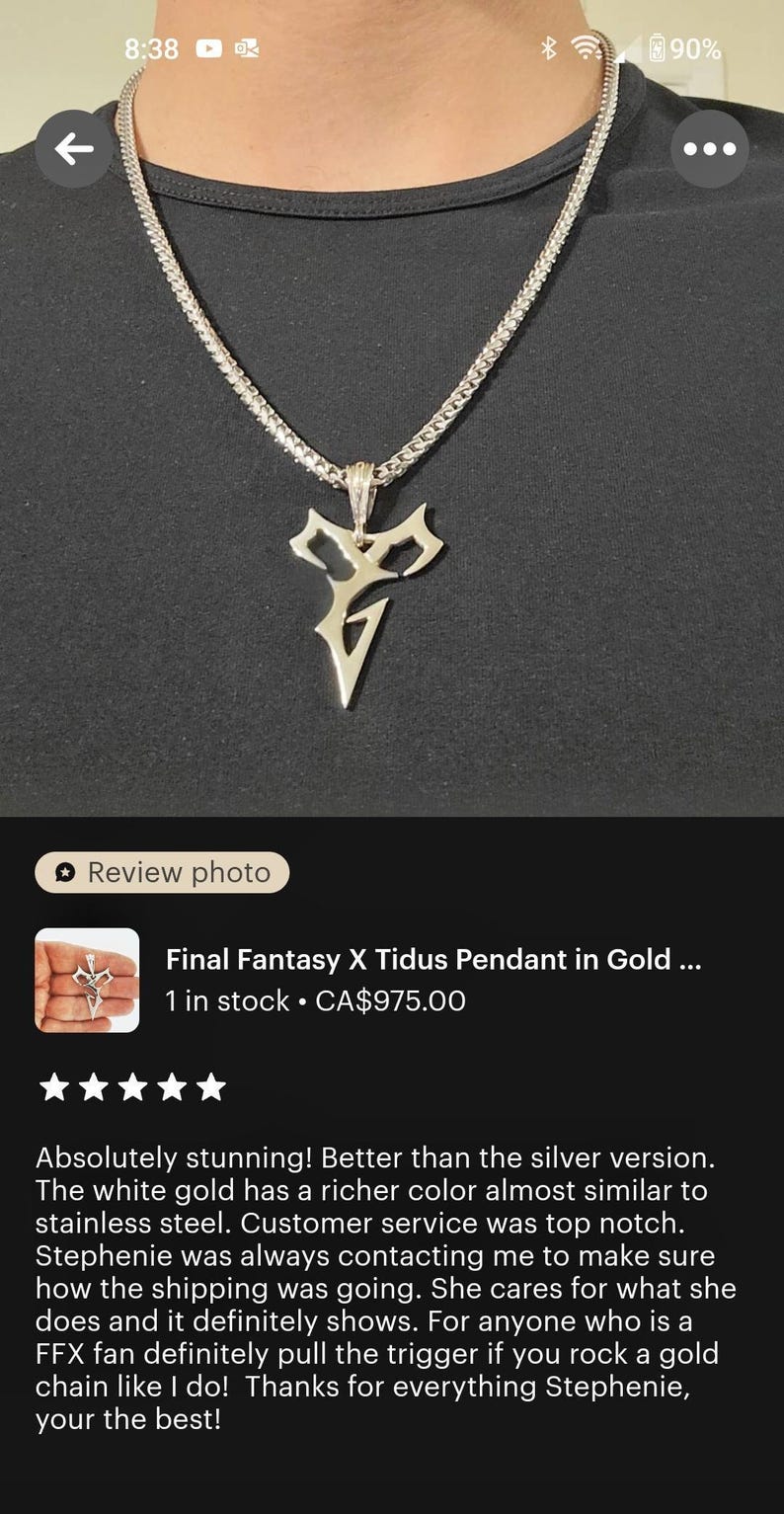 a close-up view of a gold necklace with a pendant featuring a stylized letter "V" design. The necklace is displayed on a person's neck, and the image appears to be a review photo of the necklace.