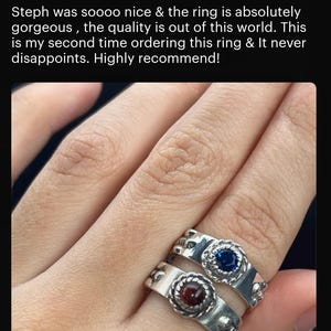 A close-up image of a person's hand wearing a silver ring with two gemstones, one blue and one red. The person is described as having a "calcifer Fire Band" in the image.