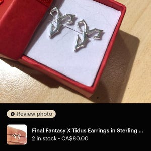 a pair of earrings in a red box, which appears to be a gift box. The earrings are described as "Final Fantasy X Tidus Earrings in Sterling" and are in perfect condition. The earrings are in stock and cost $80.00. The image also includes a review rating of 4 stars, indicating that the earrings are in excellent condition and the seller is very happy with the product.