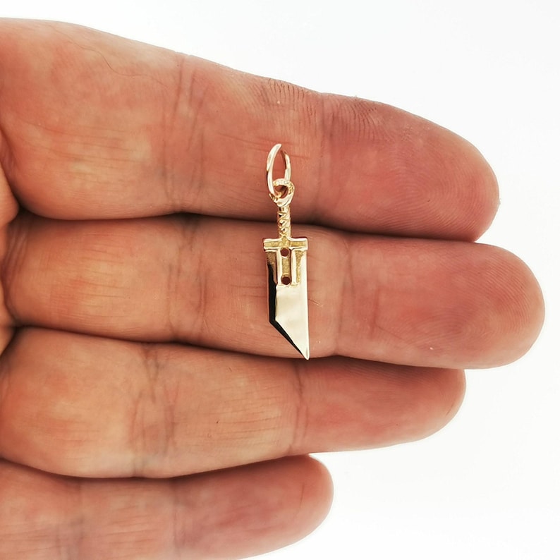 Antique bronze Cloud Strife sword charm from FFVII Final Fantasy gamer jewelry. Small FF7 Buster Sword charm in antique bronze Final Fantasy Cloud Strife pendant. Close up of small Buster Sword pendant in bronze FF7 inspired cosplay accessory. Mini Final Fantasy sword charm in bronze Cloud Strife cosplay gift