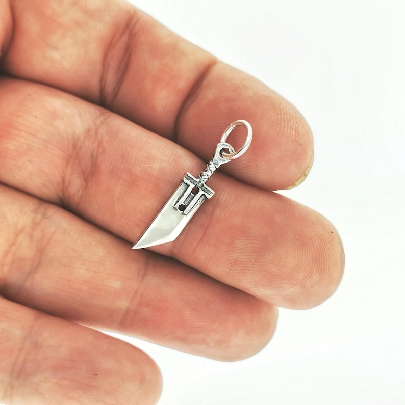 Small FF7 Buster Sword charm in sterling silver Final Fantasy Cloud Strife pendant. Close up of small Buster Sword pendant in silver FF7 inspired cosplay accessory. Mini Final Fantasy sword charm in sterling silver Cloud Strife cosplay gift.