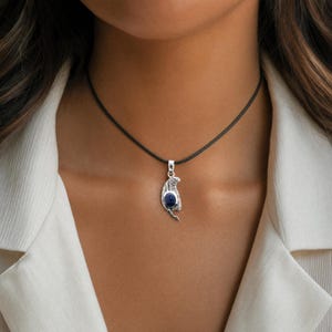 A close-up of a woman's neck wearing a silver necklace with a pendant featuring a blue gemstone.