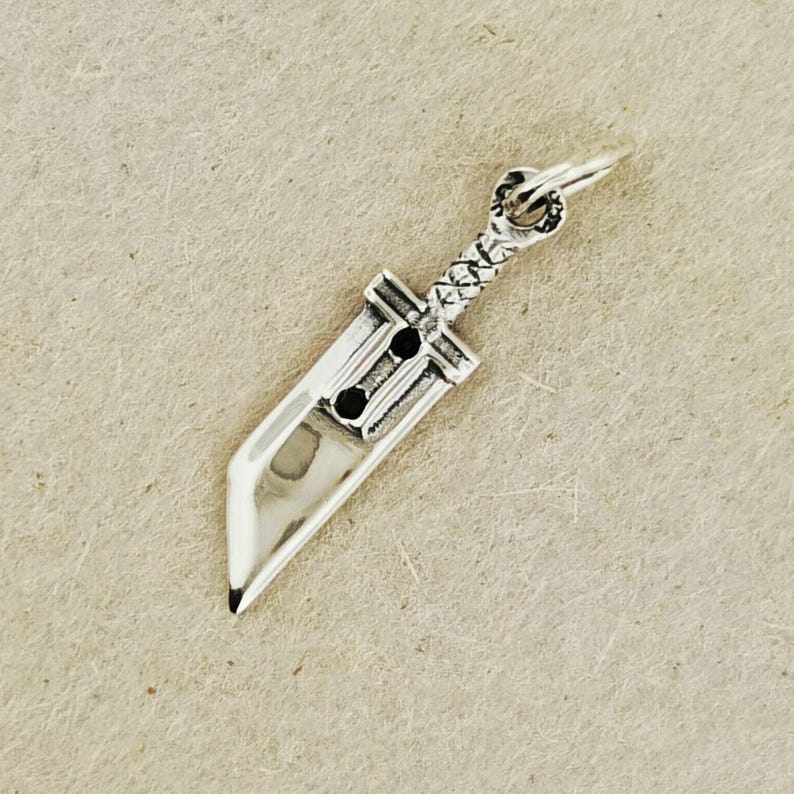Small FF7 Buster Sword charm in sterling silver Final Fantasy Cloud Strife pendant. Close up of small Buster Sword pendant in silver FF7 inspired cosplay accessory. Mini Final Fantasy sword charm in sterling silver Cloud Strife cosplay gift.