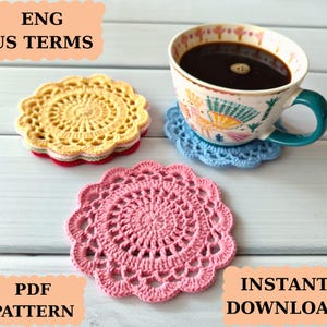May include: A cup of coffee sits on a blue crocheted coaster, with additional crocheted coasters in yellow and pink nearby. The coasters are circular with a scalloped edge. Text in the image reads "ENG US TERMS", "PDF PATTERN", and "INSTANT DOWNLOAD".