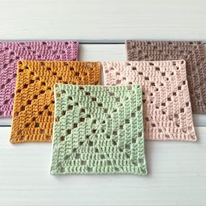 May include: Five square crochet coasters in a granny square pattern. The set includes one piece each in light pink, dusty rose, mustard yellow, sage green, and brown. Each coaster features a central flower motif with openwork stitches.