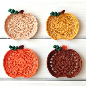 Puede incluir: Cuatro posavasos de calabaza de ganchillo en tonos beige, amarillo, naranja y marrón. Cada posavasos presenta un diseño circular con un tallo y hojas verdes. Posavasos hechos a mano para decoración otoñal.