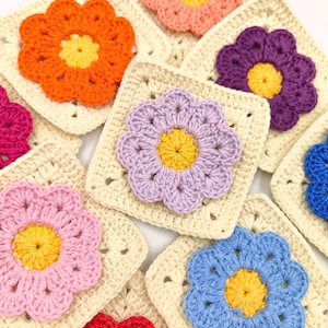 Puede incluir: Una colección de cuadrados de flores de ganchillo en varios colores, incluyendo rosa, morado, azul, naranja y rojo. Cada cuadrado presenta una gran flor de ganchillo con un centro amarillo.