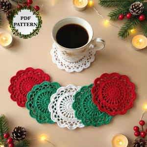 May include: A cup of coffee sits on a white crocheted coaster. Several red, green, and white crocheted coasters are arranged below. The image includes candles, pine needles, berries, and the text "PDF PATTERN".