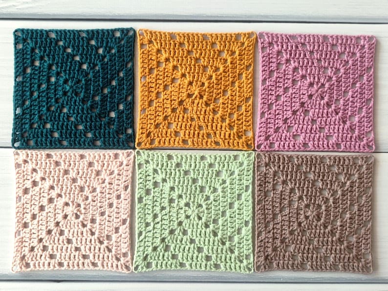 May include: Six square crochet coasters arranged in two rows of three. The colours include dark teal, mustard yellow, dusty pink, light blush, sage green, and taupe. Each piece features a classic openwork granny square pattern with yarn stitches.