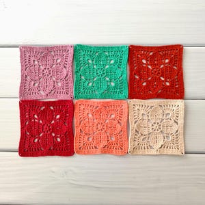 May include: A collection of six square crochet pieces in various colors, including pink, green, red, coral, and beige. Each piece features a floral design in the center and is arranged on a white wooden surface.