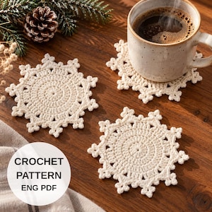 May include: Three off-white crochet coasters shaped like snowflakes, with one coaster placed under a ceramic mug filled with dark coffee. A white circular overlay with the black text CROCHET PATTERN ENG PDF is positioned in the lower left corner.