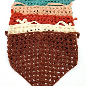 May include: A stack of six crocheted triangular scarves in various colors, including brown, cream, red, peach, and teal.
