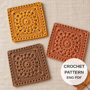 Puede incluir: Tres motivos cuadrados de ganchillo en amarillo mostaza, naranja quemado y marrón oscuro, cada uno con un diseño floral central con puntos texturizados. Una superposición circular blanca incluye el texto CROCHET PATTERN ENG PDF.