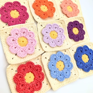 Puede incluir: Nueve cuadrados de ganchillo con un diseño de flor en varios colores, incluyendo rosa, morado, azul, rojo y naranja. Cada cuadrado tiene un centro amarillo y está rodeado por un borde blanco.