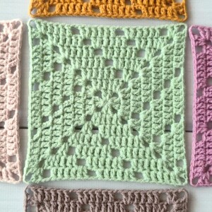 May include: A collection of five square crochet granny squares in various colours including mustard yellow, light green, pale pink, mauve, and dusty brown. Each square features a central cluster pattern with open spaces and a repeating stitch design.