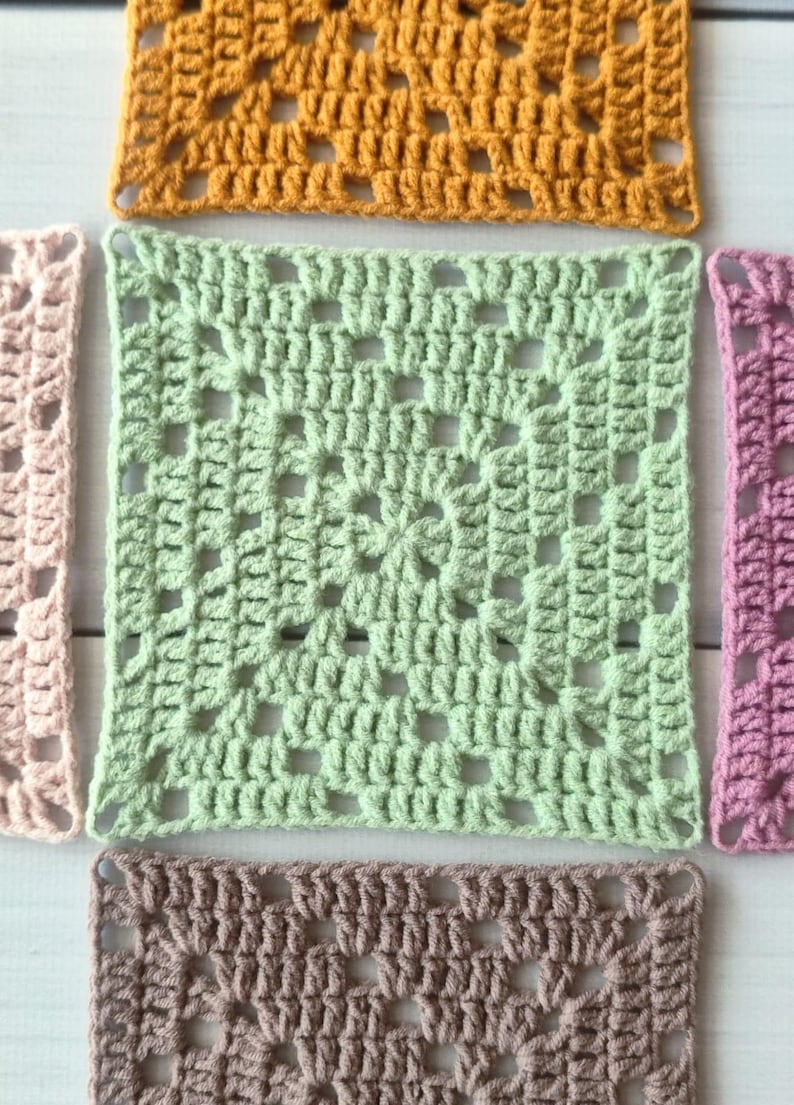 May include: A collection of five square crochet granny squares in various colours including mustard yellow, light green, pale pink, mauve, and dusty brown. Each square features a central cluster pattern with open spaces and a repeating stitch design.