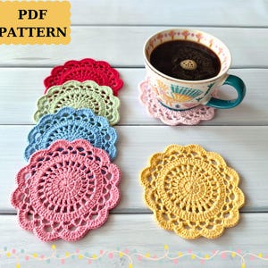 May include: A collection of colorful, crocheted coasters in red, green, blue, pink, and yellow. A cup of coffee sits on a pink coaster. The image includes the text "PDF PATTERN".