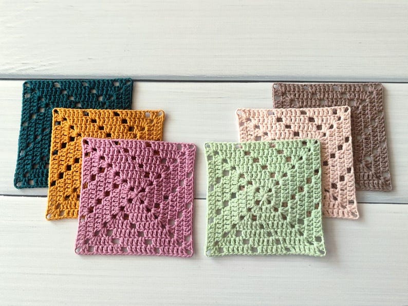 May include: A set of six square crochet coasters featuring a classic granny square pattern. The coasters are crafted in various solid colours including dark teal, mustard yellow, dusty pink, light green, pale peach, and a muted brown shade.