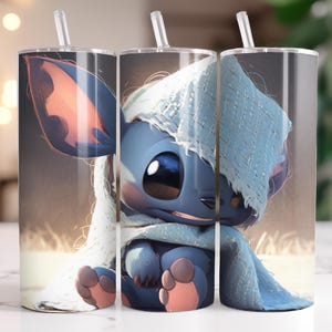 Puede incluir: Tres vasos de acero inoxidable con un personaje de dibujos animados azul, ojos grandes y una manta azul claro. Cada vaso tiene una pajita transparente y una tapa plateada. El fondo es borroso y de color neutro.