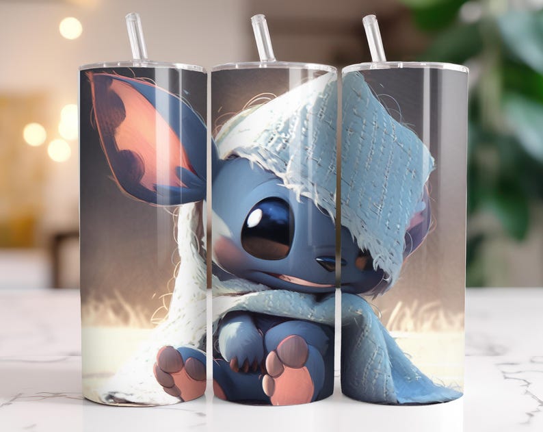 Puede incluir: Tres vasos de acero inoxidable con un personaje de dibujos animados azul, ojos grandes y una manta azul claro. Cada vaso tiene una pajita transparente y una tapa plateada. El fondo es borroso y de color neutro.