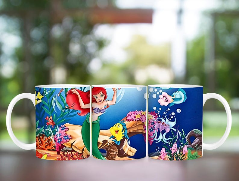 Puede incluir: Taza de cer&aacute;mica blanca con una colorida ilustraci&oacute;n de Ariel, Flounder y Sebasti&aacute;n de La Sirenita. El dise&ntilde;o incluye escenas submarinas con corales, peces y burbujas. La taza tiene un asa blanca.