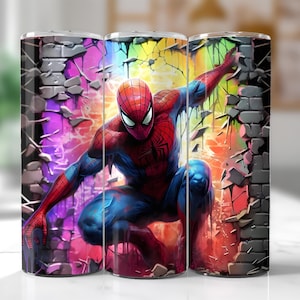 以下が含まれることがあります： スパイダーマンの鮮やかなイラストが描かれたステンレス鋼タンブラー。デザインは、虹色の背景を持つレンガの壁を突き破る、ダイナミックなポーズのスパイダーマンを示しています。タンブラーは円筒形です。