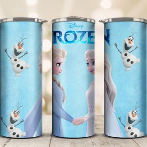 May include: A set of three stainless steel tumblers featuring characters from Disney's Frozen. The tumblers have a light blue background with images of Elsa, Anna, and Olaf. The word "Frozen" is displayed in a blue, stylized font.