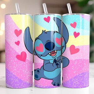 Puede incluir: Tres vasos de acero inoxidable con pajitas. Cada vaso presenta un dise&ntilde;o colorido con un personaje de dibujos animados, Stitch, rodeado de corazones rosas. El fondo tiene un patr&oacute;n de arco&iacute;ris pastel.