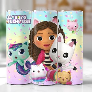以下が含まれることがあります： Gabby's Dollhouseのキャラクターが描かれたステンレス製のタンブラー3個セット。タンブラーは、ギャビーと彼女の猫の友達を背景に、パステルレインボーの背景が特徴です。「Gabby's Dollhouse」の文字がタンブラーの1つに印刷されています。