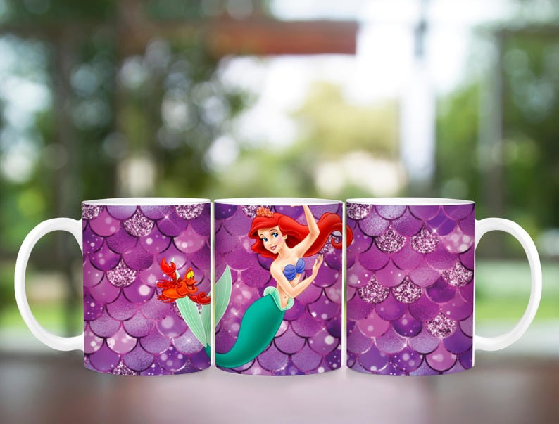 Puede incluir: Tres tazas de cer&aacute;mica blanca con un patr&oacute;n de escamas moradas e im&aacute;genes de Ariel de La Sirenita. Una taza presenta a Ariel con un cangrejo y las otras tazas muestran el patr&oacute;n de escamas con detalles brillantes.