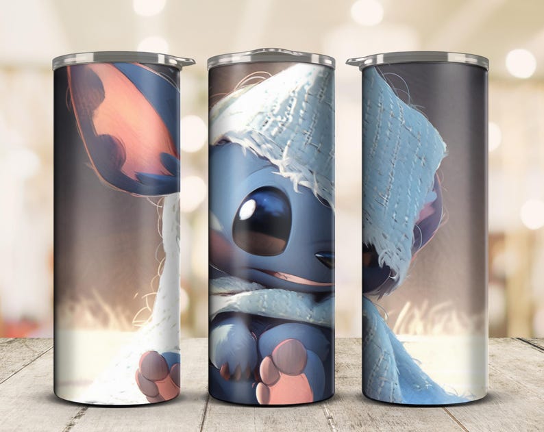May include: A set of three stainless steel insulated tumblers. Each tumbler features a full-wrap design of a blue cartoon character wearing a light blue hat and scarf. The character has large eyes and pink ears and feet. The background is a blurred brown.