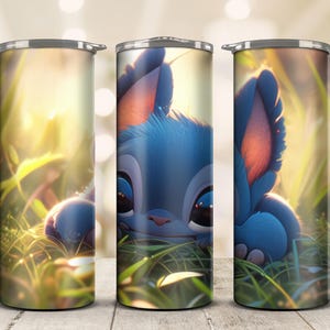 May include: A set of three stainless steel tumblers featuring a blue cartoon character in a grassy field. The character has large ears, big eyes, and a blue and pink color scheme. The background is a soft, blurred image of sunlight and greenery.