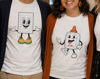 May include: Four people wearing white t-shirts with cartoon graphics of a pencil, a piece of paper, a glue bottle, and scissors. The person on the left holds a clipboard with the text "TEACHERS MAKE A MARK" and wears a pumpkin-patterned skirt.