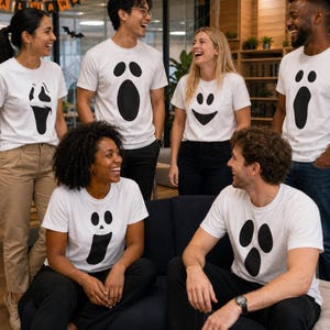 May include: A group of six white t-shirts featuring various black ghost face graphics. Each shirt displays a unique expression, including wide-eyed, screaming, and smiling ghost faces printed on the front of the short-sleeved cotton garments.
