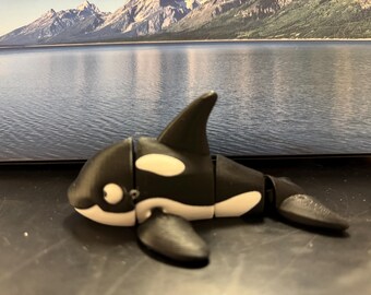 May include: A black and white orca figurine with a segmented body. The figurine is made of plastic and has a realistic design.