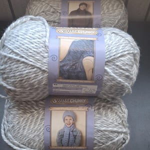 May include: Three skeins of gray and white chunky yarn are stacked. Each skein has a label with a picture of a person wearing a knitted item. The labels read "Softies Chunky" and include free pattern information.