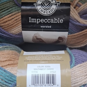 May include: A close-up of two skeins of Loops & Threads Impeccable worsted yarn in the Southwest Ombre colorway. The yarn is a blend of blue, green, tan, and purple. The label indicates the yarn is medium weight and machine washable.