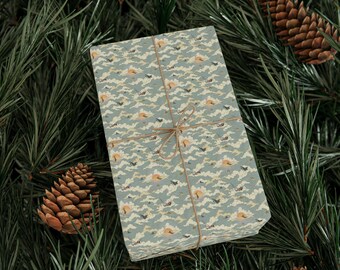 May include: A wrapped gift box with a patterned paper featuring clouds, birds, and suns in shades of blue, beige, and orange. The box is tied with twine and rests on a bed of green pine needles, with pine cones scattered around.