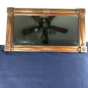May include: A rectangular wall mirror featuring a medium-toned wooden frame with turned spindle accents along the top and bottom edges. The four corners of the frame are adorned with square blocks that each feature a circular floral carving.