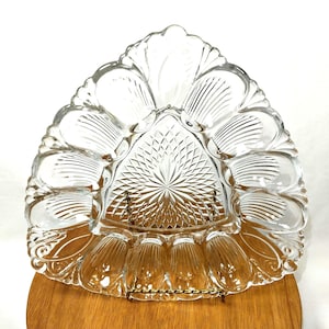 May include: A triangular clear glass serving platter featuring twelve individual recessed oval compartments arranged around a central triangular section with a pressed diamond and starburst pattern, finished with a scalloped edge.