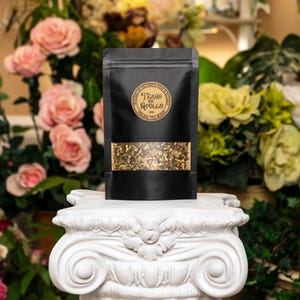 May include: A black pouch with a clear window showing a blend of dried herbs. The pouch has a gold label with the text "Tears of Apollo Herbal Tea Blend".