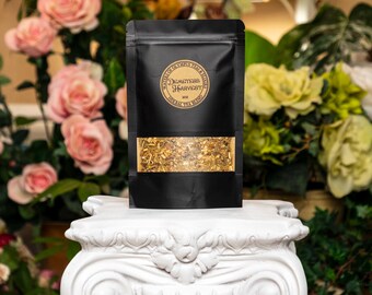 Może przedstawiać: Czarny woreczek z złotą etykietą z napisem "Demeter's Harvest" Herbal Tea Blend 30g. Woreczek jest wypełniony luźną herbatą i stoi na białym cokole.