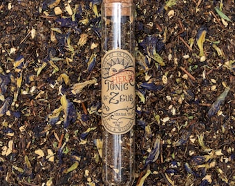 Może przedstawiać: Szklana probówka wypełniona luźną herbatą ziołową. Etykieta zawiera napis "Propert's Herbal Tonic of Zeus, Herbal Tea, Net Wt 1 oz, Focus & Wisdom".