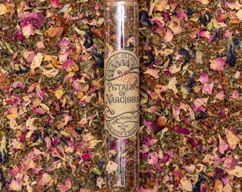 Może przedstawiać: Szklana probówka wypełniona mieszanką suszonych ziół i płatków kwiatów, z etykietą "Petals of Narcissus Herbal Tea - Skin Glow & Beauty".